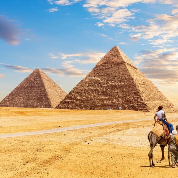 Turistas montando camellos frente a las pirámides de Giza.