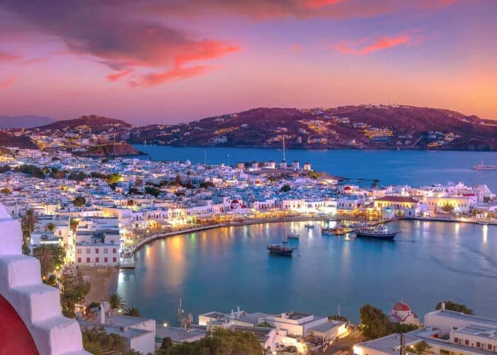 Vista nocturna de una ciudad griega iluminada con luces brillantes.