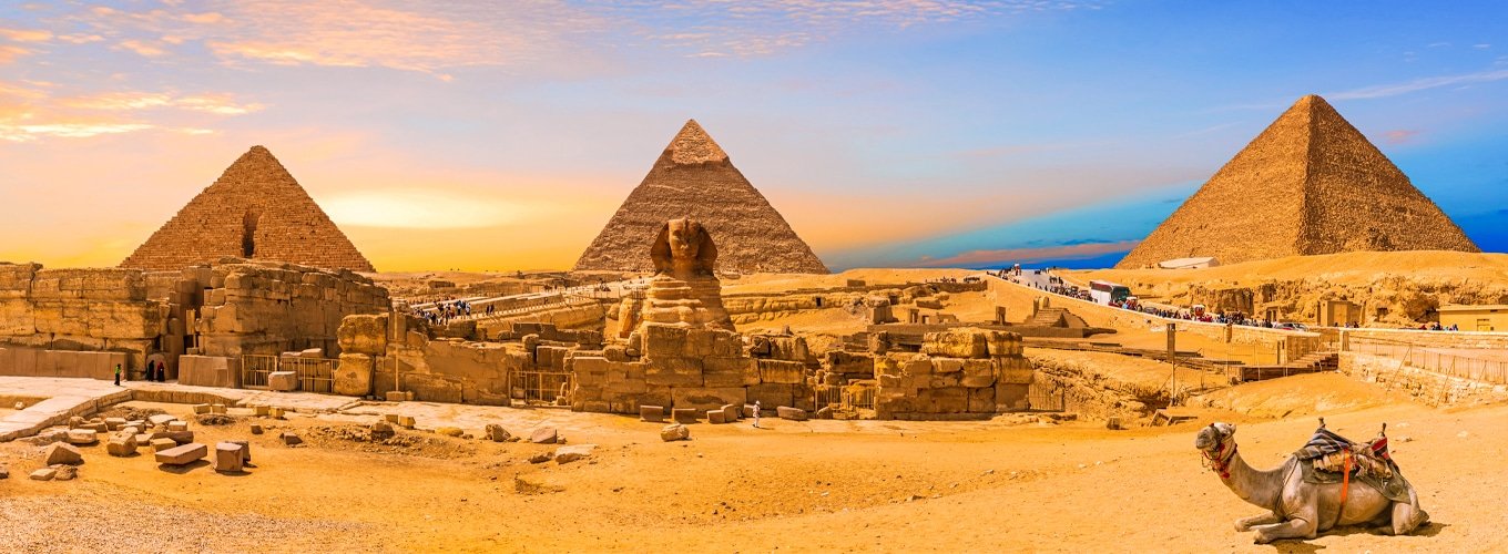 giza-pirámides-esfinge-panorama-con-camello-acostado-por-el cairo-egipto Vista panorámica de las pirámides de Giza y la Esfinge con un camello acostado en El Cairo.