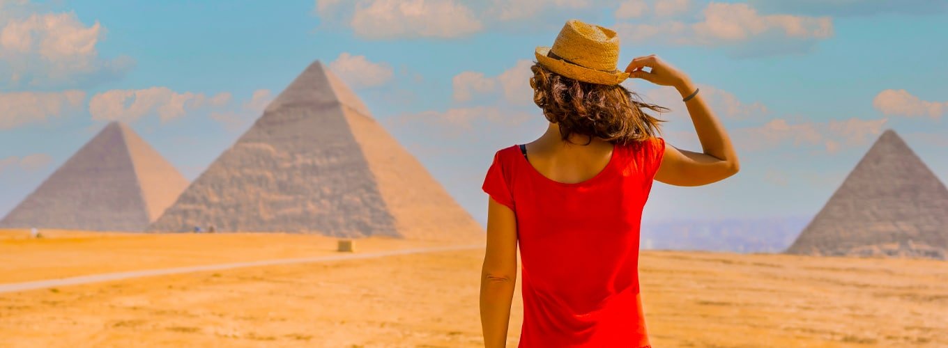 Mujer joven con vestido rojo frente a las pirámides de Giza bajo un cielo nublado.