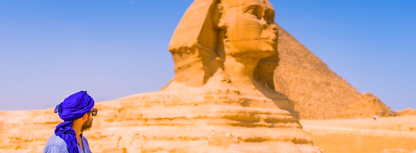 Turista joven cerca de la Gran Esfinge de Giza, con vestimenta azul y turbante azul.