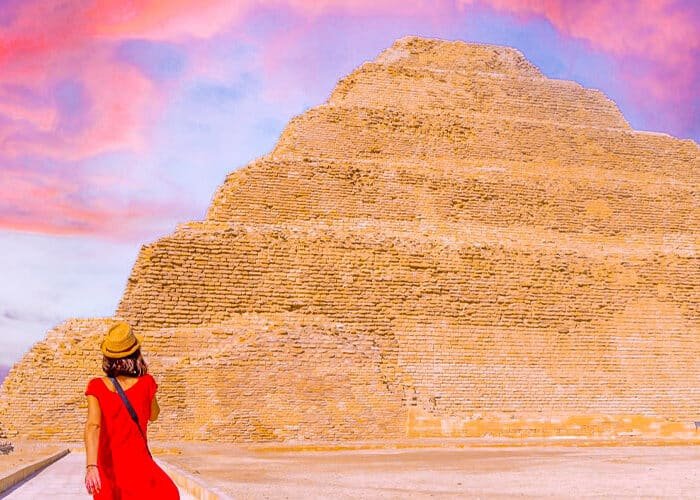 Turista con vestido rojo frente a la pirámide de Zoser al atardecer.