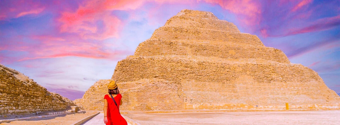Turista con vestido rojo frente a la pirámide de Zoser al atardecer.