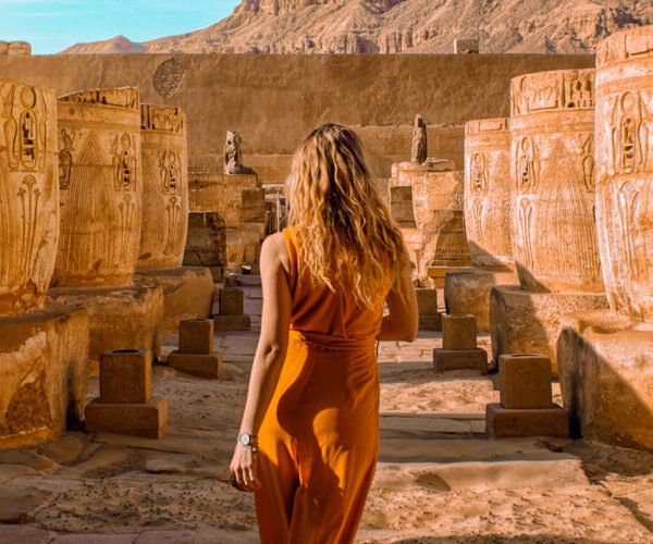 Turista extranjero junto a columnas de templo egipcio en un paisaje impresionante.