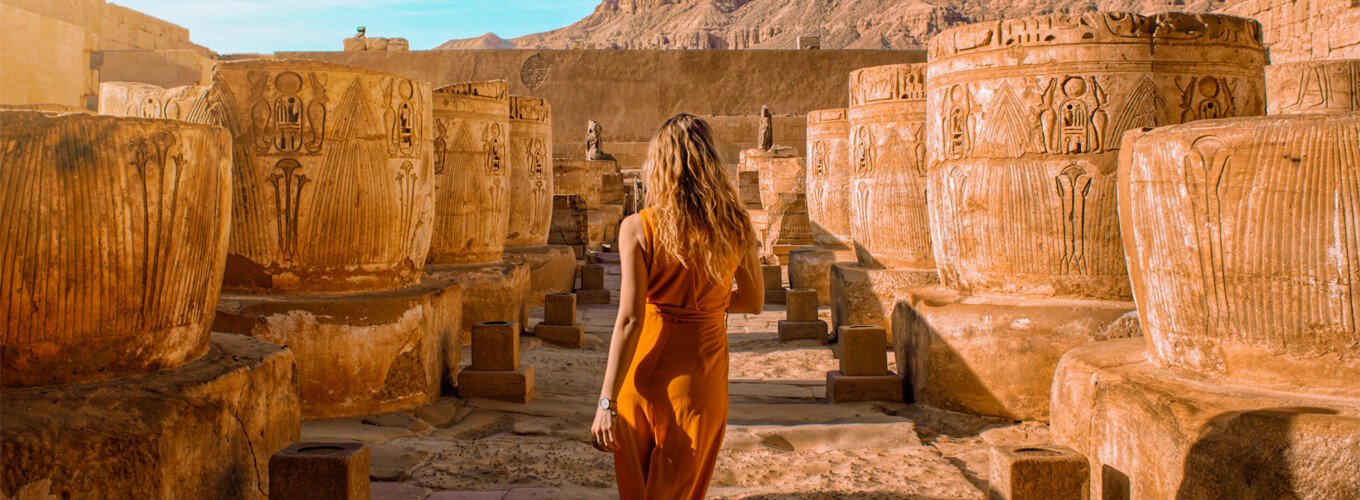 Turista extranjero junto a columnas de templo egipcio en un paisaje impresionante.