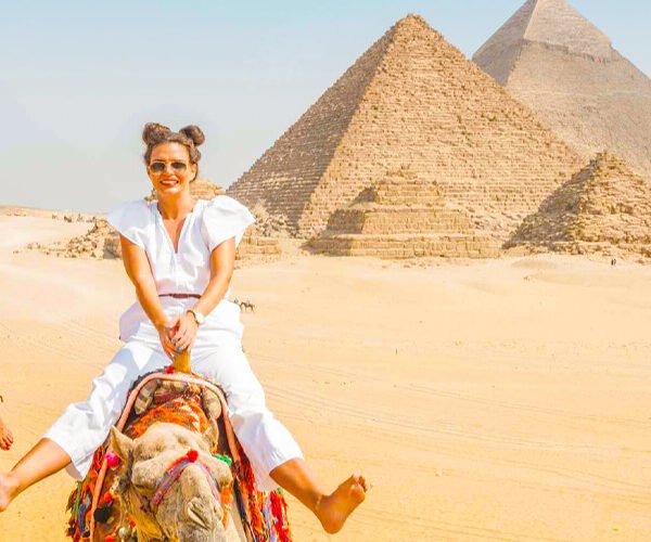 Dos niñas montando un camello frente a las pirámides de Egipto.