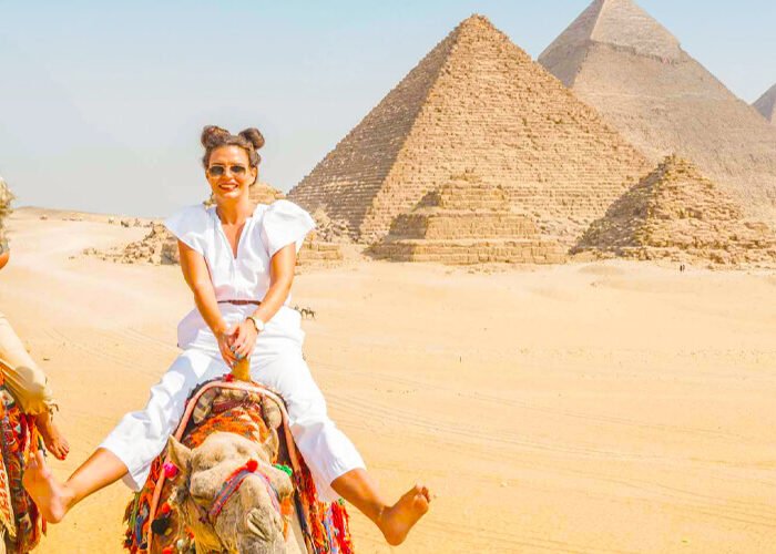 Dos niñas montando un camello frente a las pirámides de Egipto.