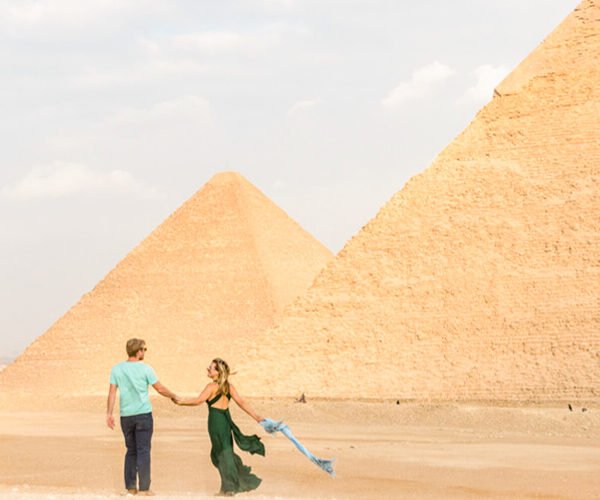 Pareja sonriendo frente a las pirámides de Egipto.