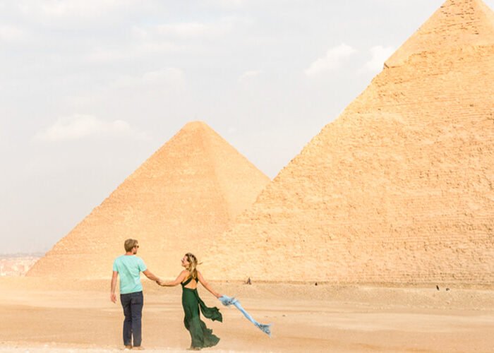 Pareja sonriendo frente a las pirámides de Egipto.