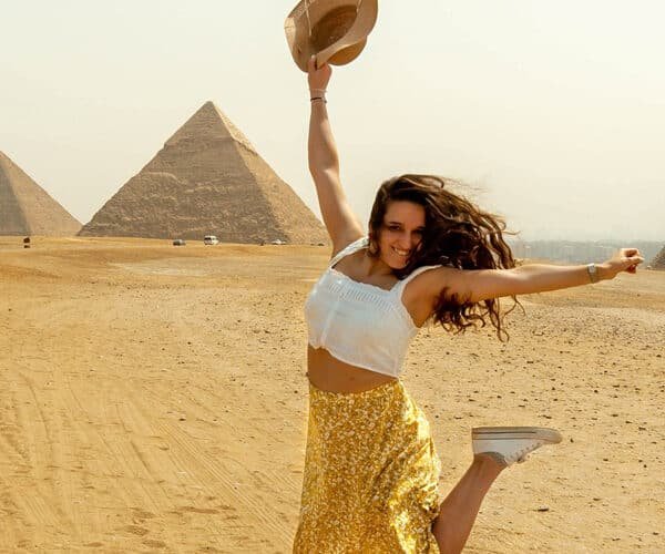 Turista extranjera saltando alegremente frente a las pirámides de Egipto.