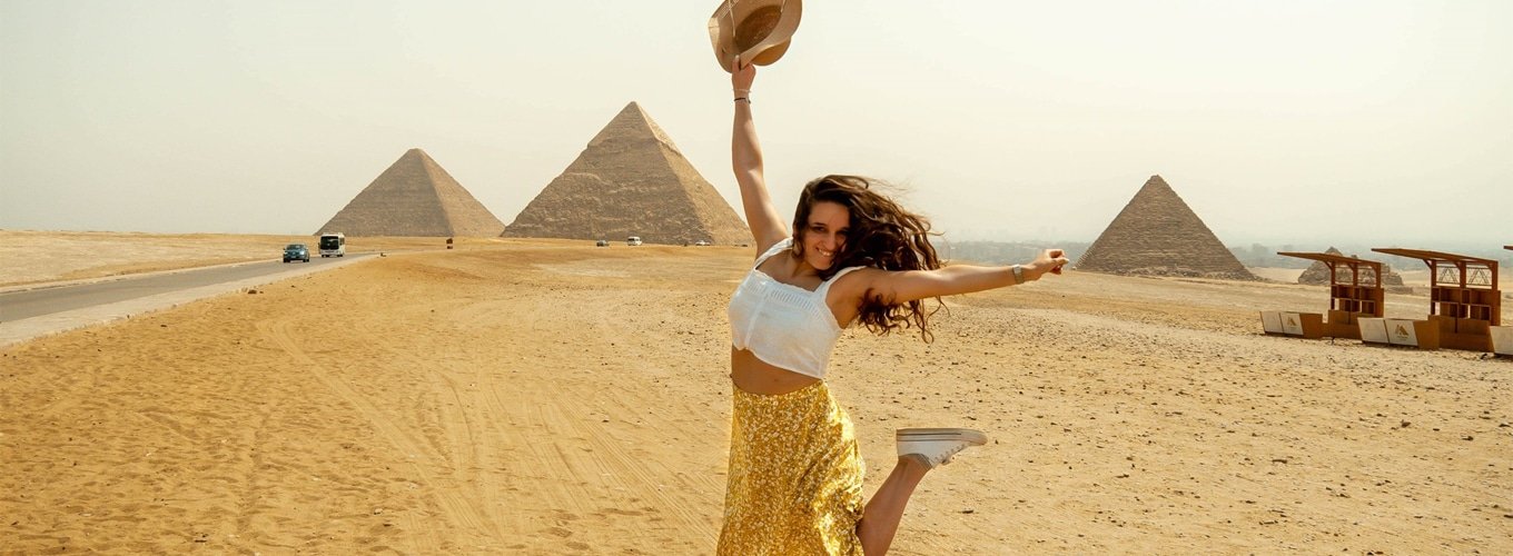 Turista extranjera saltando alegremente frente a las pirámides de Egipto.